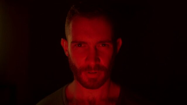 Angry man open eyes, awakes in hell, looking at camera with fury, rage, his face lit with fire flames, grief, sorrow. Male starring at enemy on war with aggresive emotions and insane devilish look.