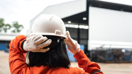 An unrecognized construction worker is wearing a white safety helmet or hardhat with factory place...