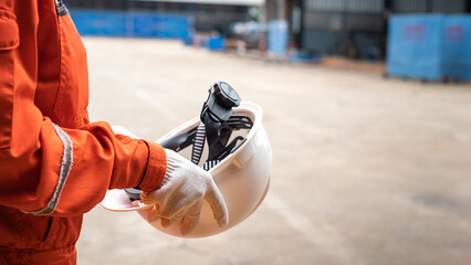 Fototapeta premium Action of a worker is preparing to wear a white safety hardhat with blurred background of factory workplace. Industrial safe work practice concept photo, selective focus.