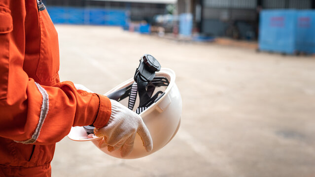 Action of a worker is preparing to wear a white safety hardhat with blurred background of factory workplace. Industrial safe work practice concept photo, selective focus.