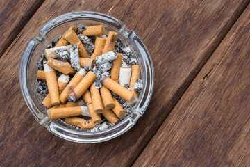 Top view of many cigarette stubs and ash in a glass ashtray