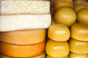 Cheese heads of different colors and sizes are stacked on counter. Fair trade in homemade cheese, market. Close-up. Selective focus.