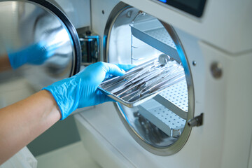 Woman hand in gloves puts dental instrument into sterilization apparatus