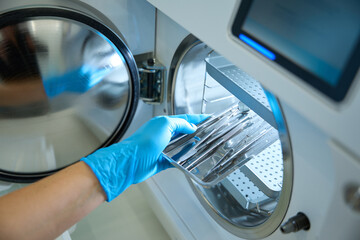 Hand in gloves puts dental instrument on shelves of sterilizer