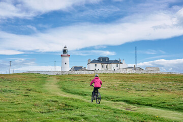 nice senior woman on mountain bike, cycling at Dunmore Head Lighthouse near Kilballyowen , County Limerick in the southwestern part of the Republik of Ireland