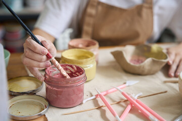 Woman dips a brush into a jar of pink paint
