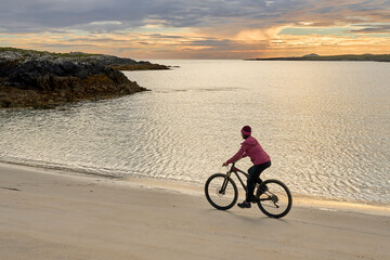 Fototapeta na wymiar nice senior woman on mountain bike, cycling in sunset at the golden sand beach of Sillerna, Grallagh, County Galway, in the western part of the Republic of Ireland