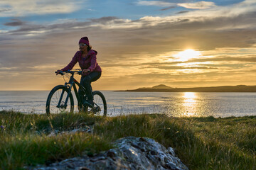 Fototapeta premium nice senior woman on mountain bike, cycling in sunset in the sand dunes of Sillerna, Grallagh, County Galway, in the western part of the Republic of Ireland