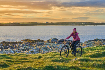Obraz premium nice senior woman on mountain bike, cycling in sunset on the cliffs of Sillerna, Grallagh, County Galway, in the western part of the Republic of Ireland