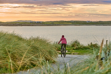 nice senior woman on mountain bike, cycling in sunset in the sand dunes of Sillerna, Grallagh,...