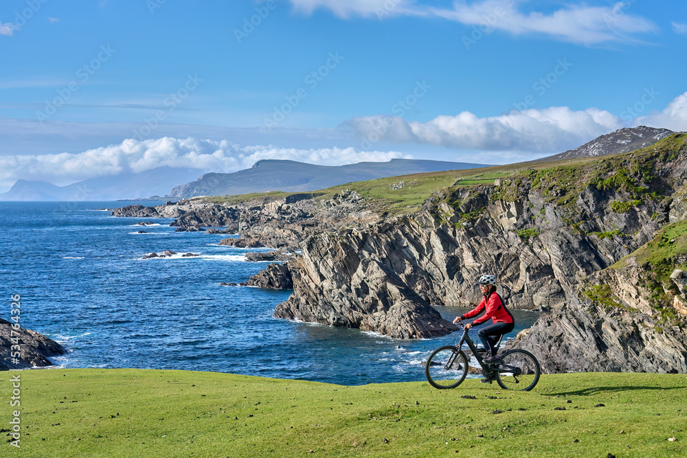 Wall mural nice senior woman on mountain bike, cycling on the cliffs of achill island, carrowgarve, republik of