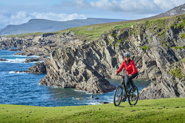 Fototapeta premium nice senior woman on mountain bike, cycling on the cliffs of Achill Island, Carrowgarve, Republik of Ireland