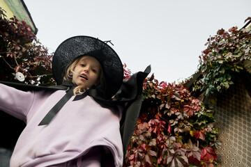 Portrait of little cute girl in witch costume and hat for halloween on fall autumn leaves background. Happy Halloween.
