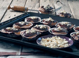 Homemade cupcakes in paper forms, covered with chocolate icing and sprinkled with coconut.