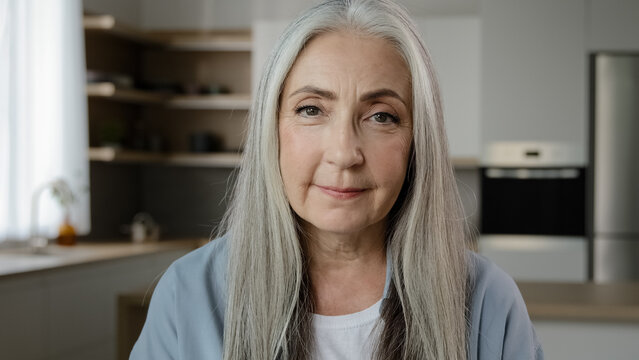 Portrait calm confident adult middle-aged woman pensioner granny mistress homeowner tender mature old lady with long grey hair posing in kitchen room serene looking at camera healthy beauty appearance
