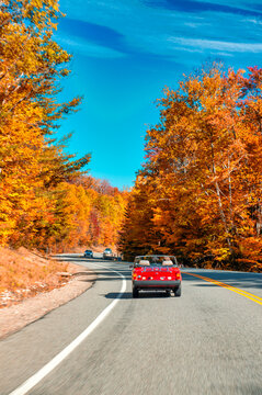 Old vintage red car driving along a road of New England in foliage season, USA