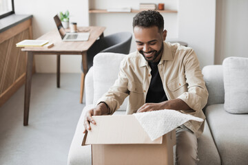 Happy man opening parcel at home, handsome guy opens package indoor, delivery, shipment, satisfied...