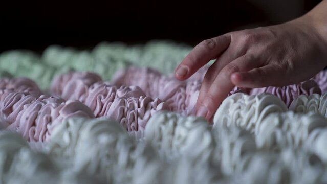 closeup hand takes two pink marshmallow cookies from big group served on table.