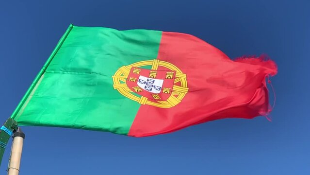 Waving flag of Portugal in windy weather with blue sky in the background. Slow motion