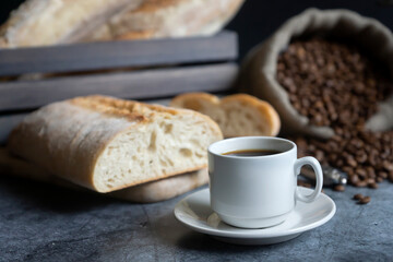 A cup of hot coffee, coffee beans and fresh white bread on a dark background.