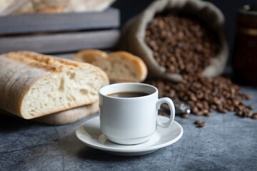A cup of hot coffee, coffee beans and fresh white bread on a dark background.