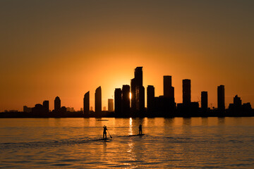 Stand up paddle boarders in the water at sunset with a city skyline silhouette in the background. Humber Bay, Toronto Ontario