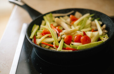 Cooking in the kitchen at home in a pan of fresh vegetables cut into strips: cherry tomato, zucchini, red pepper, eggplant