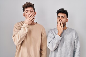 Young homosexual couple standing over white background bored yawning tired covering mouth with hand. restless and sleepiness.