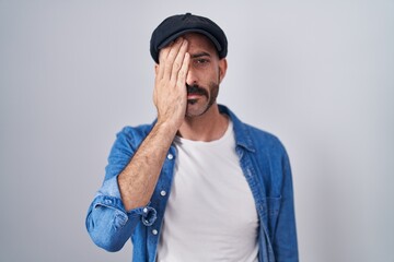 Hispanic man with beard standing over isolated background yawning tired covering half face, eye and mouth with hand. face hurts in pain.