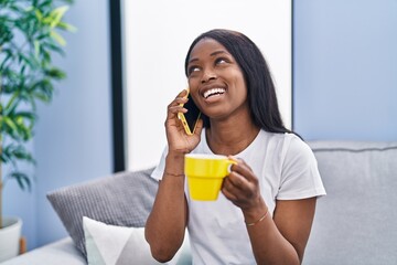 Young african american woman talking on the smartphone drinking coffee at home