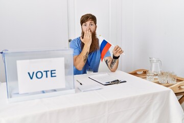 Caucasian man with long beard at political campaign election holding russia flag covering mouth...
