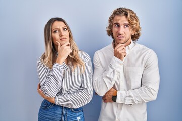 Young couple standing over blue background thinking worried about a question, concerned and nervous with hand on chin