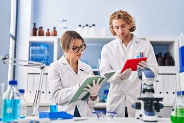 Man and woman wearing scientist uniform writing on notebook using touchpad at laboratory