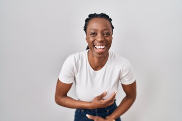 Beautiful black woman standing over isolated background smiling and laughing hard out loud because funny crazy joke with hands on body.