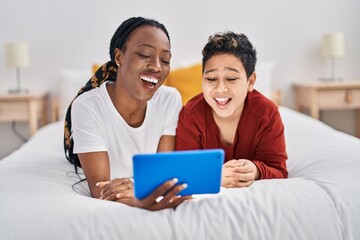 African american mother and son using touchpad lying on bed at bedroom