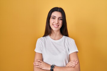 Obraz premium Young beautiful woman standing over yellow background happy face smiling with crossed arms looking at the camera. positive person.