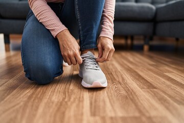 Young woman tying shoelace at home - obrazy, fototapety, plakaty