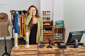 Beautiful hispanic woman working at fashion shop covering one eye with hand, confident smile on face and surprise emotion.