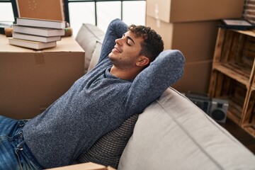 Fototapeta premium Young hispanic man relaxed with hands on head sitting on sofa at new home