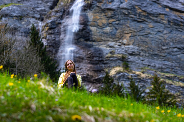 Naklejka premium sweet girl rests on a green field in a valley surrounded by mighty mountains and numerous waterfalls; valley walk in lauterbrunnen, swiss alps