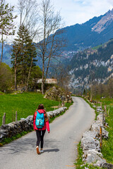 Fototapeta premium hiker girl with backpack walks through an alpine valley surrounded by mighty mountains and numerous waterfalls; valley walk in lauternbrunen, swiss alps