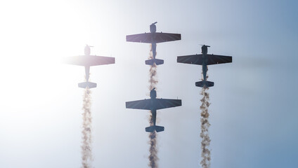 Silhouettes of training aircraft performing aerobatics on a clear sunny day.