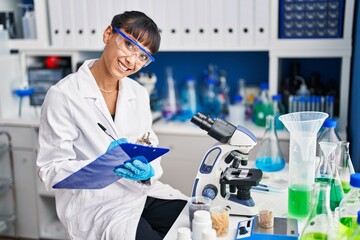 Young beautiful hispanic woman scientist smiling confident writing on document at laboratory