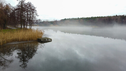 View of lake. Dry trees and yellow grass on the banks. Fog over the lake. Autumn