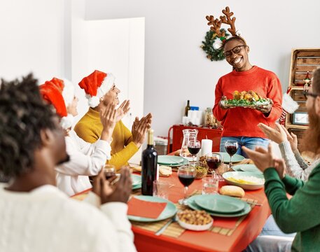 Group of people meeting clapping and sitting on the table. Woman standing and holding roasted turkey celebrating Christmas at home.