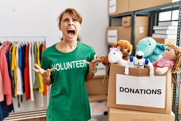 Beautiful caucasian woman wearing volunteer t shirt at donations stand crazy and mad shouting and...