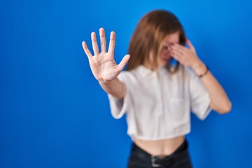 Beautiful woman standing over blue background covering eyes with hands and doing stop gesture with sad and fear expression. embarrassed and negative concept.