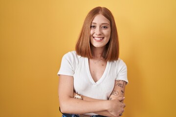 Obraz premium Young redhead woman standing over yellow background happy face smiling with crossed arms looking at the camera. positive person.