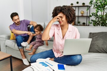 Mother of interracial family working using computer laptop at home smelling something stinky and...