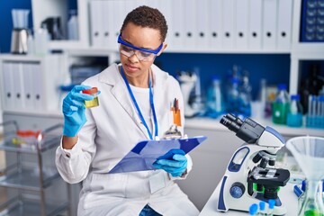 African american woman scientist holding urine test tube reading document at laboratory